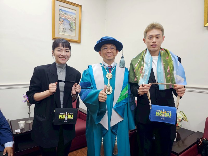 國立中山大學校長李志鵬（中）致贈羽球國手林俊易（右）及甫新婚的夫人程郁捷中山大學小書包與運動毛巾，以及出國實用的行李束帶與吊牌，祝福比賽順利。