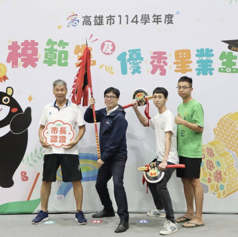岡山農工模範生暨市長獎畢業生何宇祐（右二）今天與阿公郭文賓（左一）、弟弟帶著象徵家族精神的宋江陣頭旗與雙斧，與市長陳其邁一同合影，成為現場最吸睛的畫面。